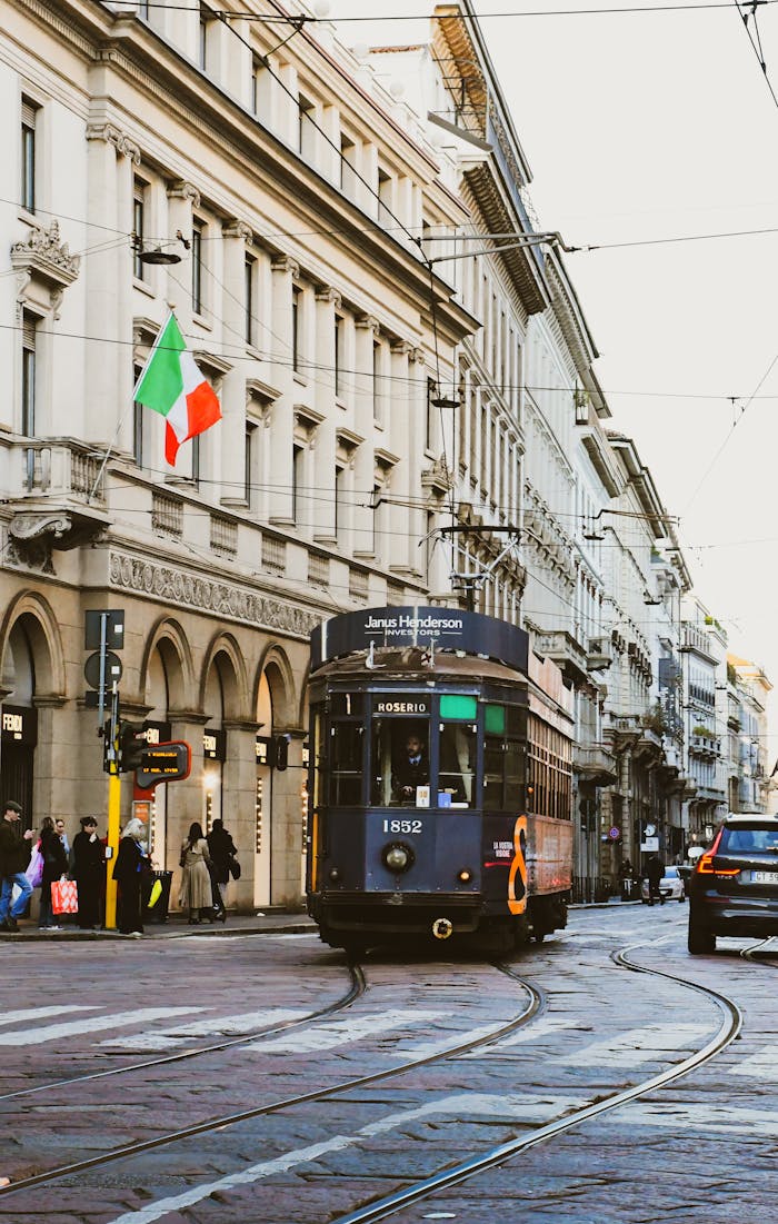 Historic electric tram navigating a bustling street in Milan, Italy, with city life and European architecture.